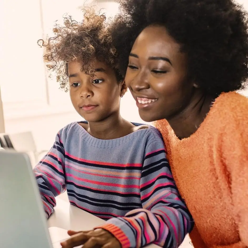 A happy mother and her focused daughter collaborate on a digital task together.