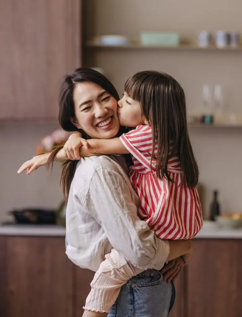 A happy mother joyfully holding her daughter while standing in the kitchen.