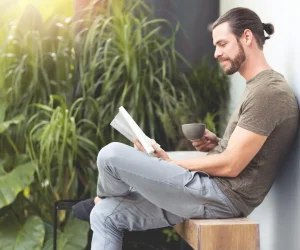 Relaxing Hipster man holding cup of coffee and reading a book at outdoor on his Vacations.