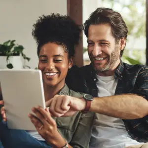 couple sitting on a couch and looking at a tablet together while laughing
