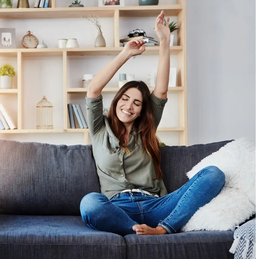 Shot of a happy young woman dancing while sitting on her sofa at home