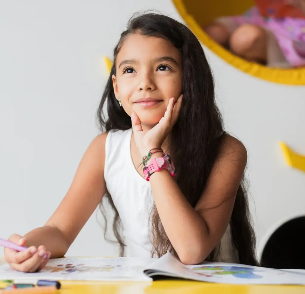 Young girl lost in thought while drawing at her kindergarten desk, expressing creativity and imagination with every colorful stroke