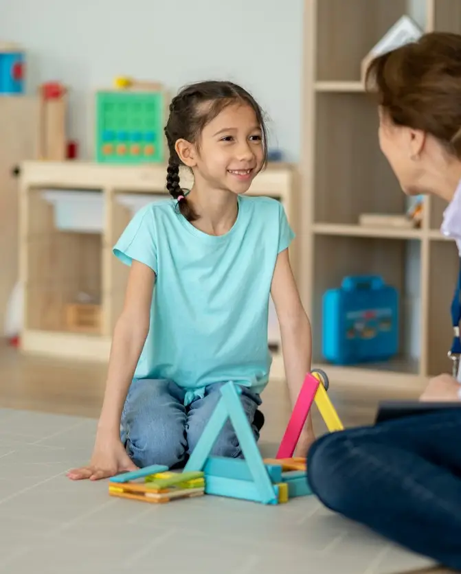 Female therapist sits on the floor with a little girl during a play therapy session.