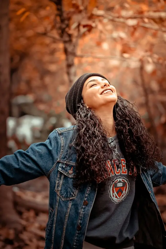 Woman in autumn leaves smiling with arms outstretched
