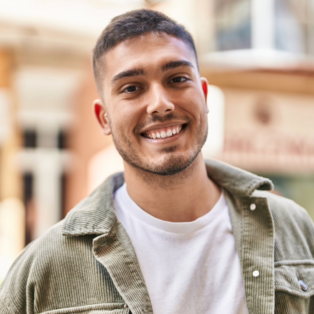 A man with short hair standing in front of a building and smiling.