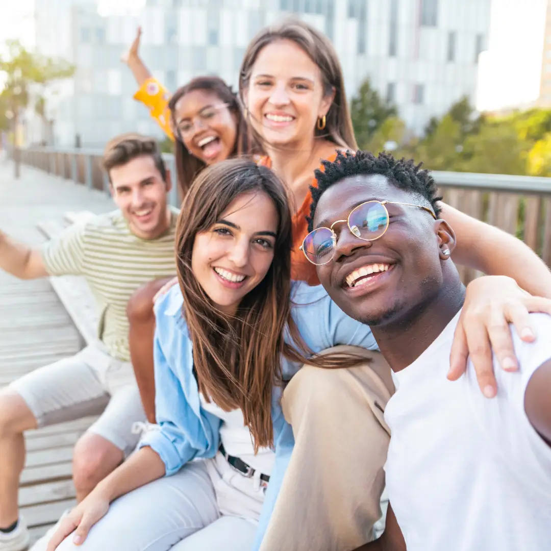 Happy friends sitting on bench taking a selfie