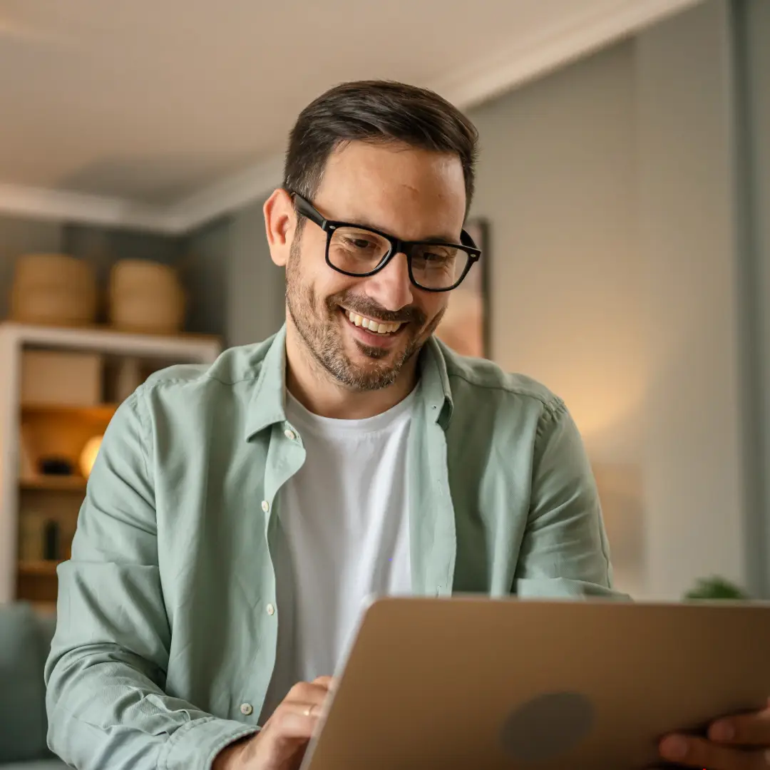 man wearing a seafoam coloured shirt and glasses smiling and looking at his laptop