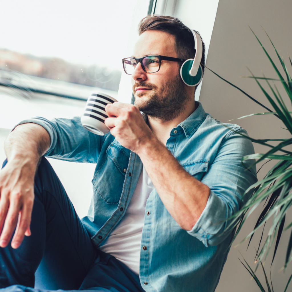 Man with glasses looking out the window and drinking tea with a pensive look