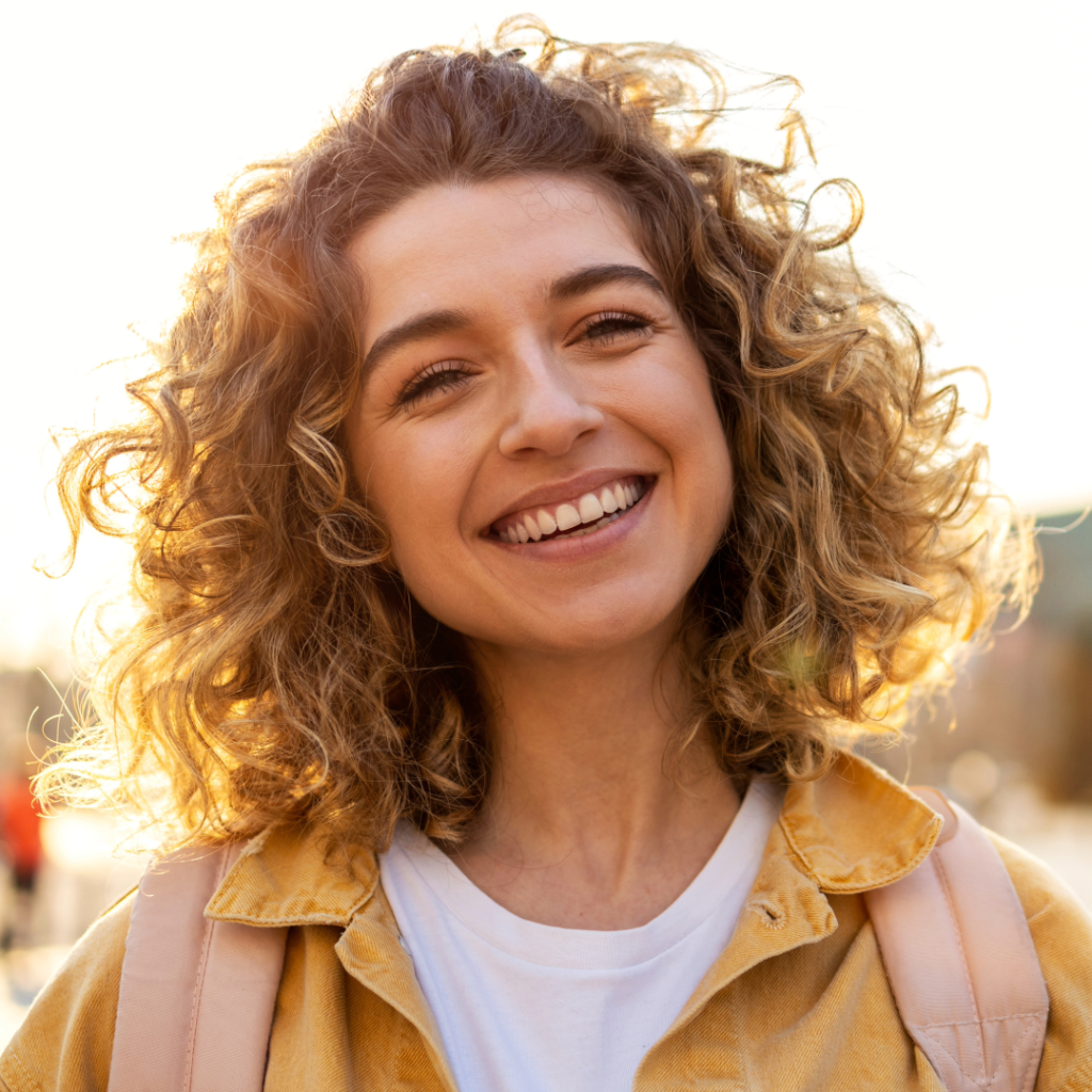 smiling young woman with curly blonde hair and a yellow jacket