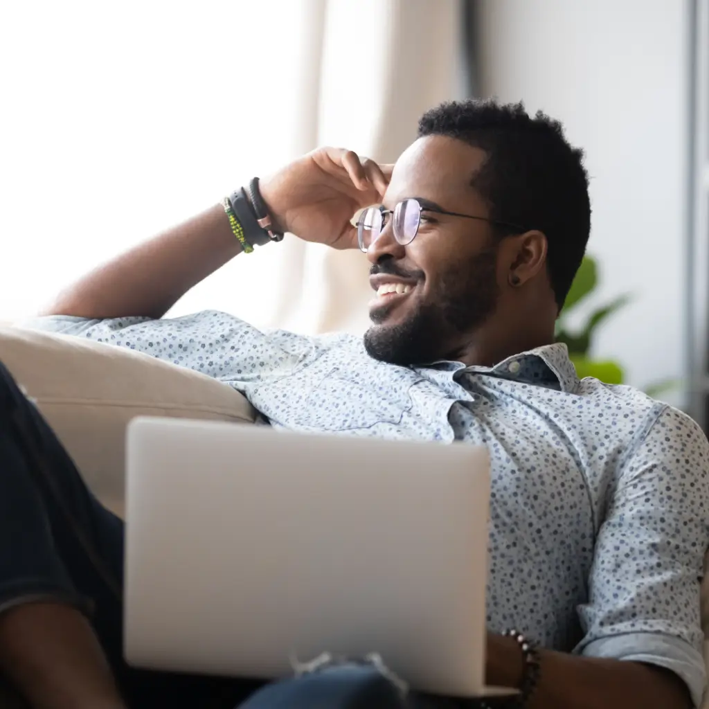 Man sitting on a couch with a laptop and looking out the window