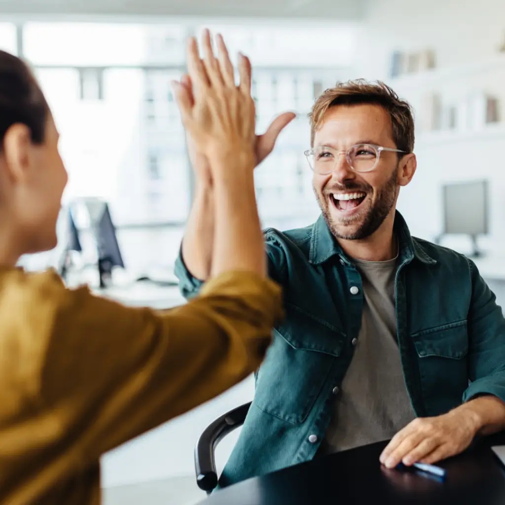 A laughing man and a woman high five each other at work