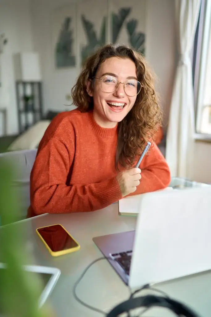 happy young woman student laughing using laptop sitting at desk studying online.